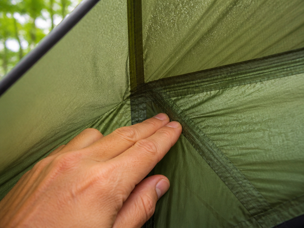 Close-up of hand checking a tent seam for dampness after washing