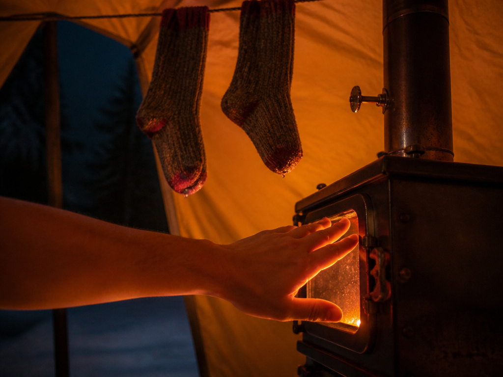 Close-up of a wood stove heating and drying gear inside a hot tent