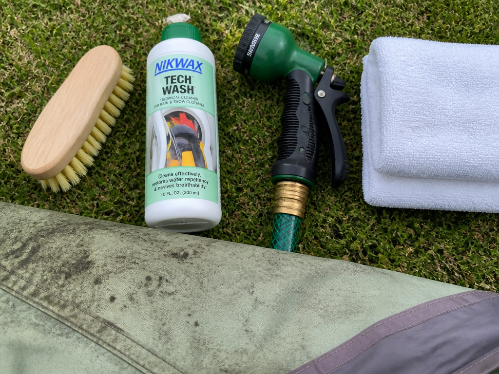 Four tools for cleaning mildew off a tent: soft brush, tech wash, hose, towels.