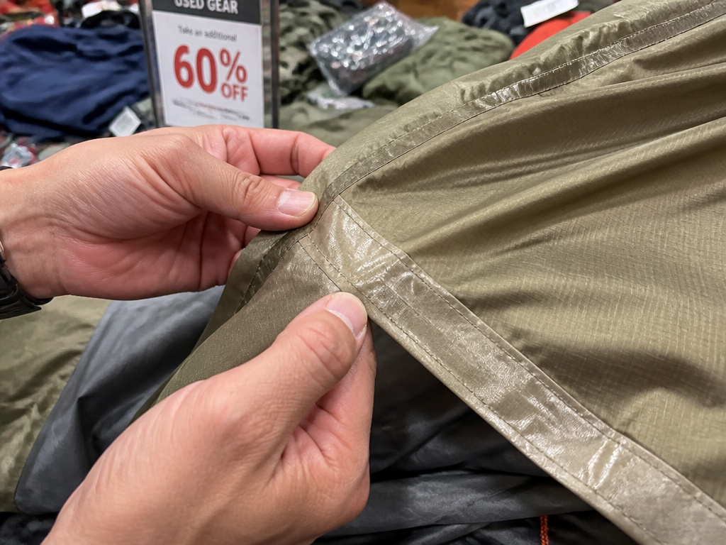Close-up inspection of a discounted tent seam at an outdoor gear sale.