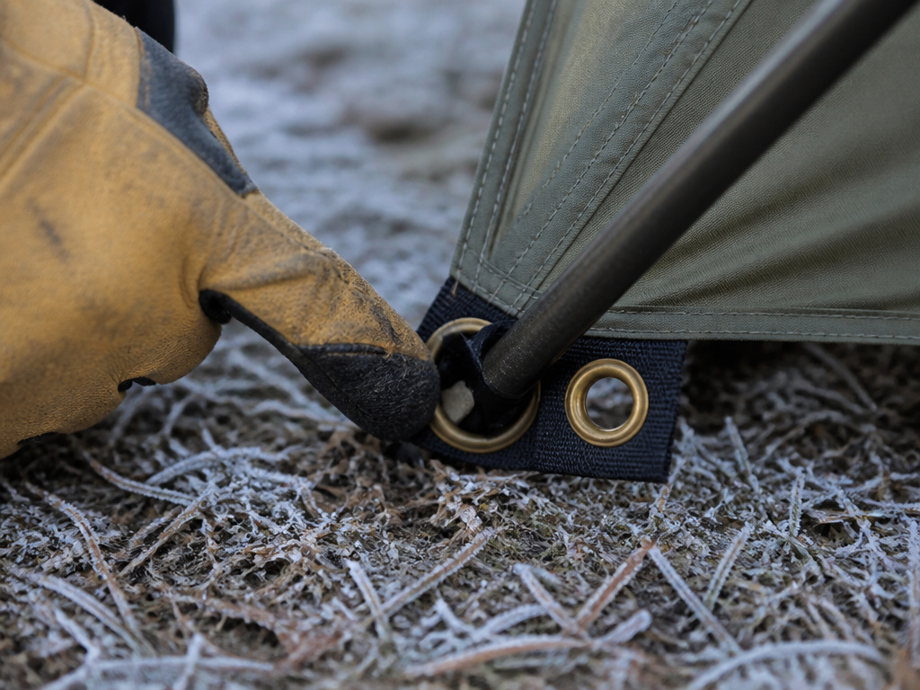Close-up of a tent pole tip in a two-grommet stake loop for fabric expansion.