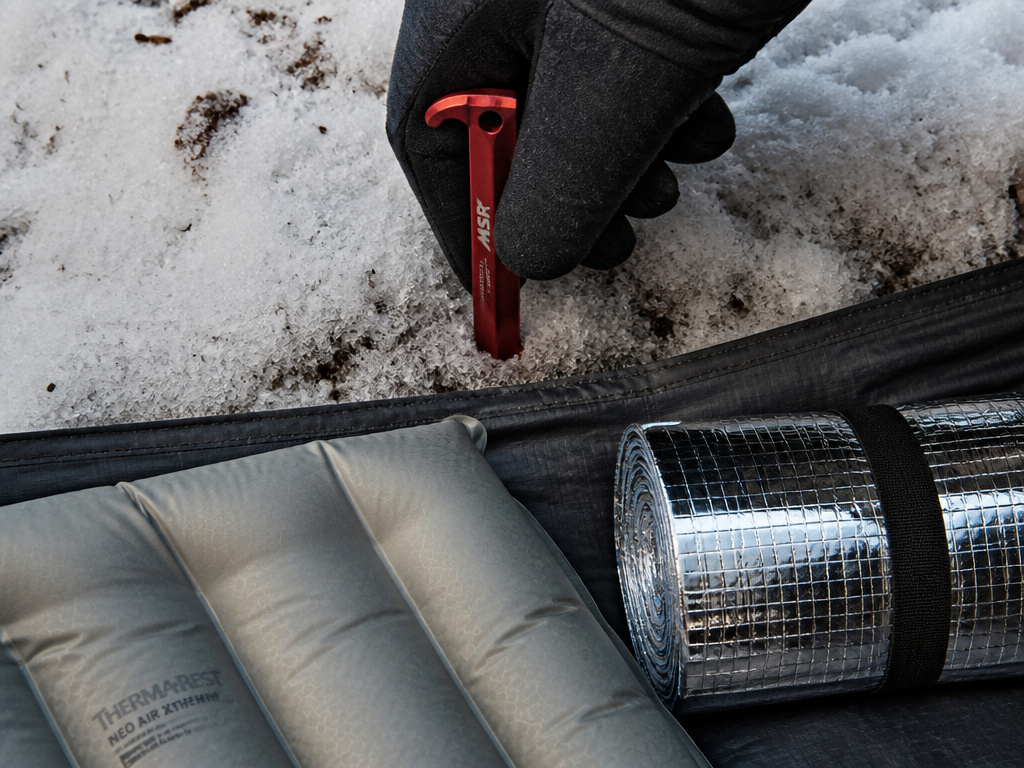 Winter tent insulation gear: snow stakes, sleeping pad, and emergency blanket.